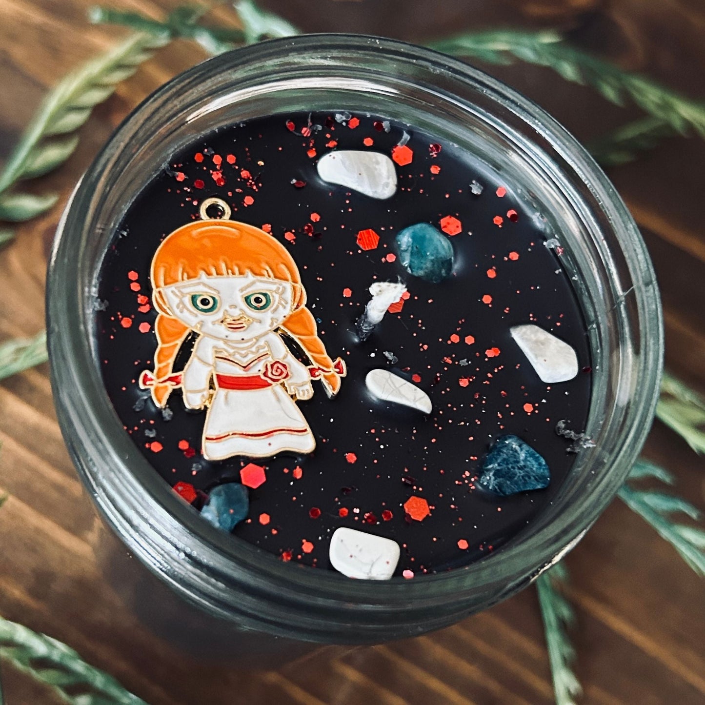A black Halloween candle that is decorated with an Annabelle horror movie charm, spooky crystals, and paranormal glitter.