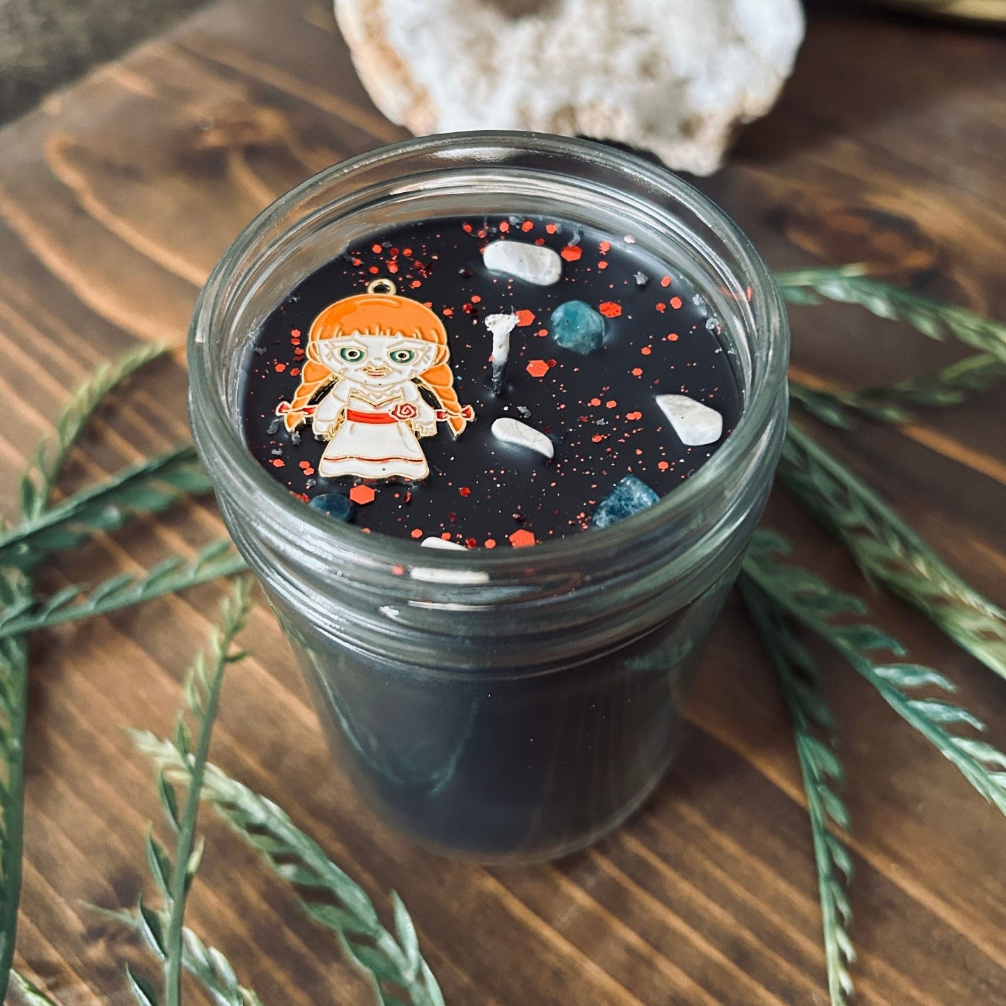 A black Halloween candle that is decorated with an Annabelle horror movie charm, spooky crystals, and paranormal glitter.