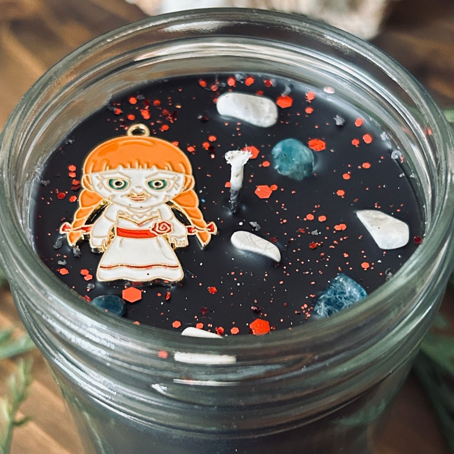 A black Halloween candle that is decorated with an Annabelle horror movie charm, spooky crystals, and paranormal glitter.