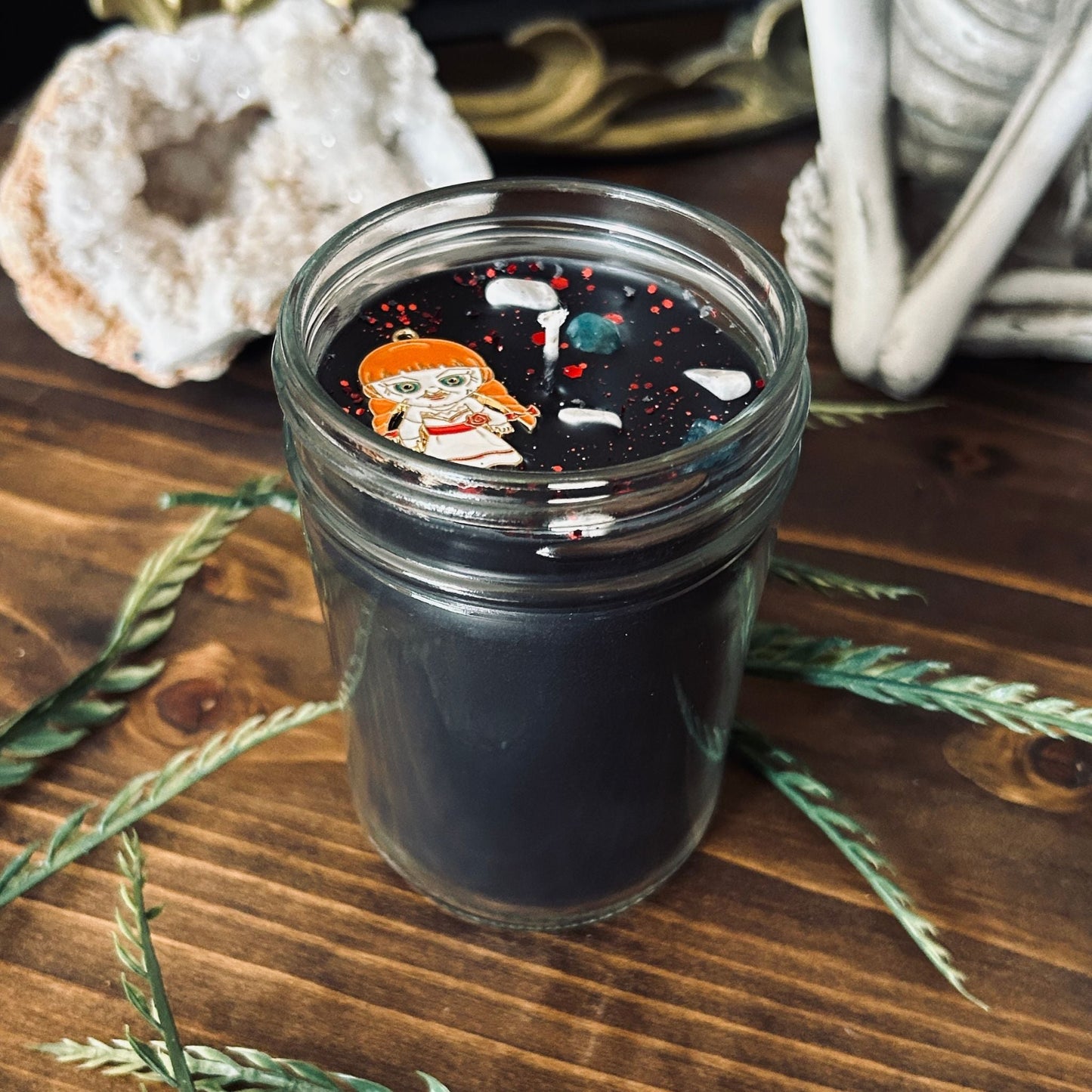 A black Halloween candle that is decorated with an Annabelle horror movie charm, spooky crystals, and paranormal glitter.