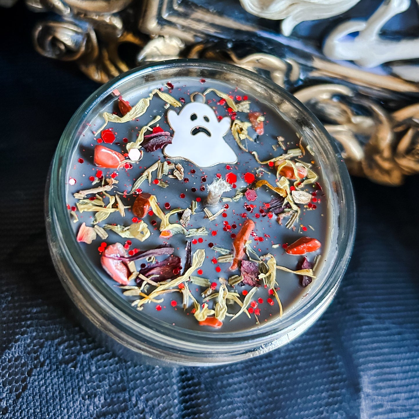 A black Halloween candle with a spooky ghost, orange crystals, and autumn leaves.