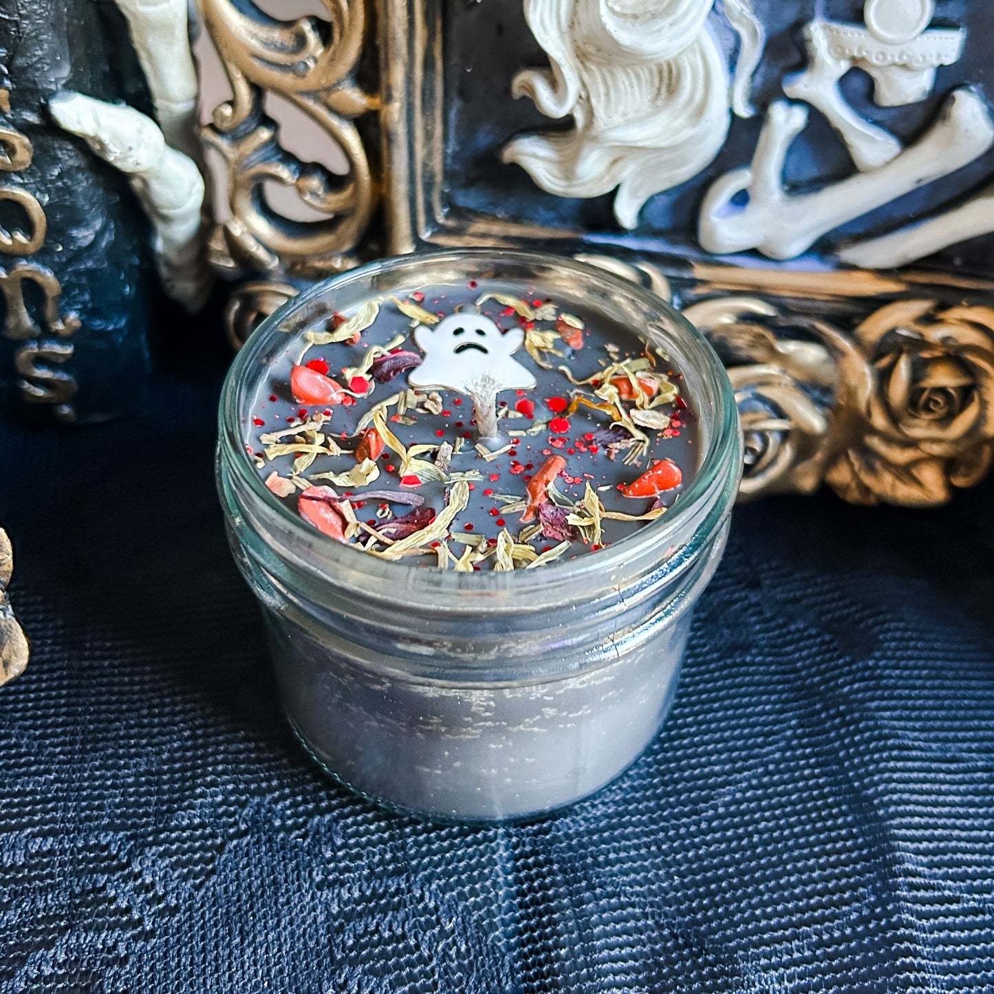 A black Halloween candle with a spooky ghost, orange crystals, and autumn leaves.