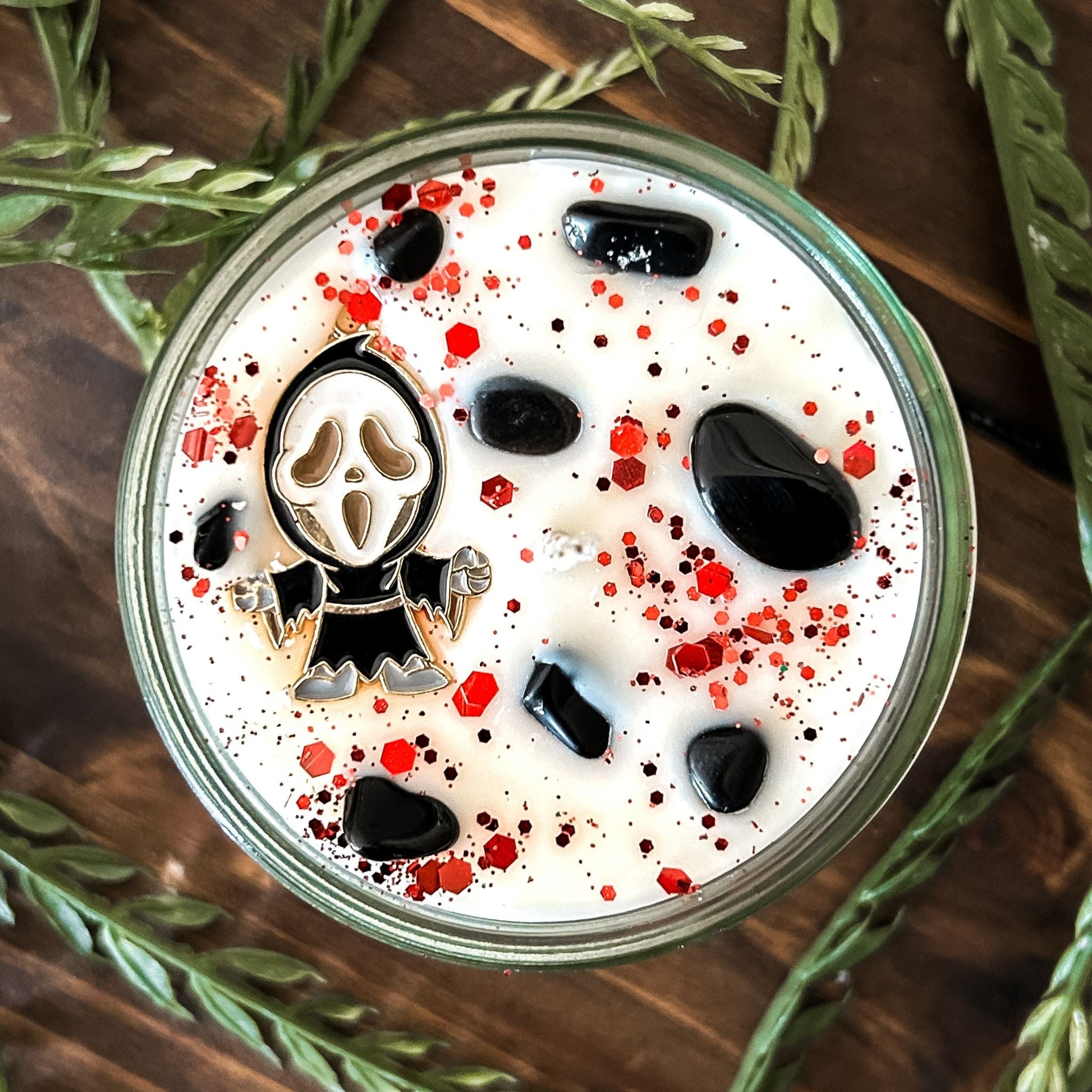 A Halloween candle decorated with a horror movie charm, spooky crystals, and gothic glitter.
