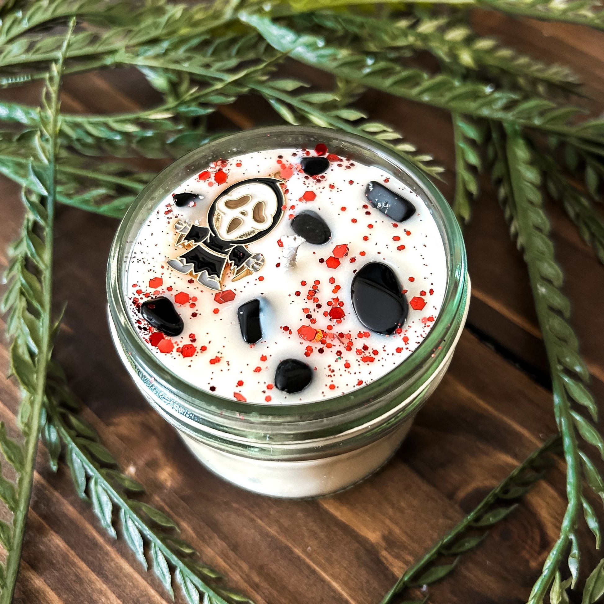 A Halloween candle decorated with a horror movie charm, spooky crystals, and gothic glitter.