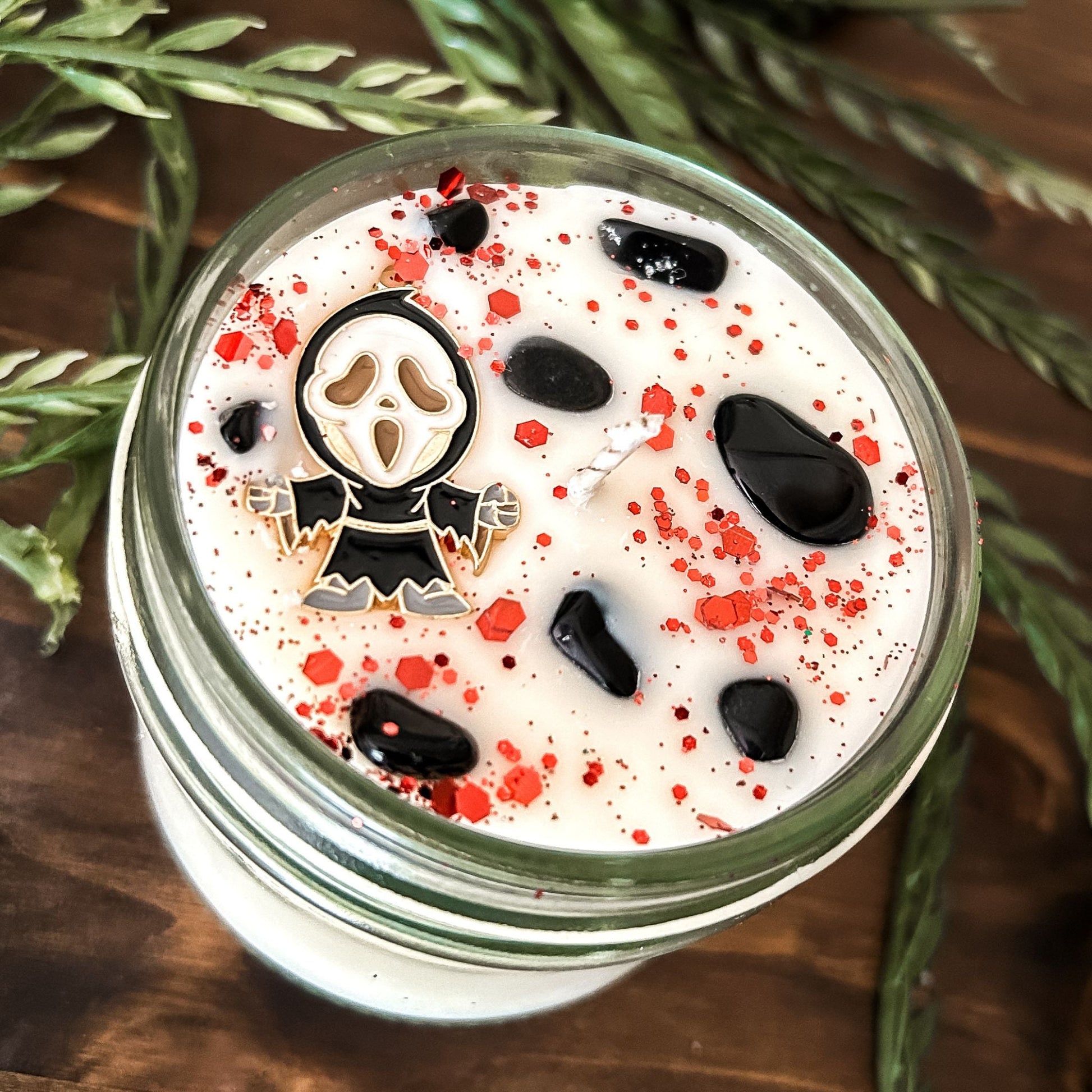 A Halloween candle decorated with a horror movie charm, spooky crystals, and gothic glitter.