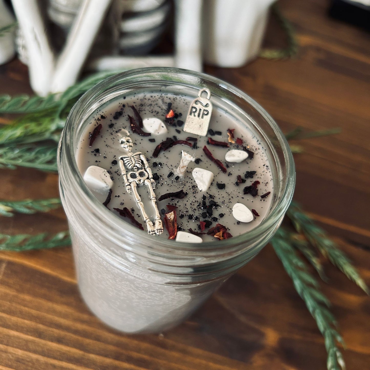 A dark Halloween candle that is decorated with a scary skeleton, a spooky rest in peace sign, white crystals, and gothic black glitter.