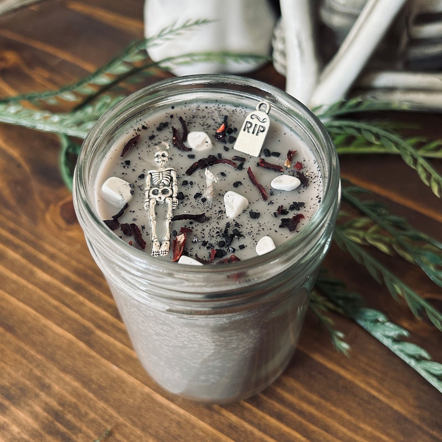 A dark Halloween candle that is decorated with a scary skeleton, a spooky rest in peace sign, white crystals, and gothic black glitter.