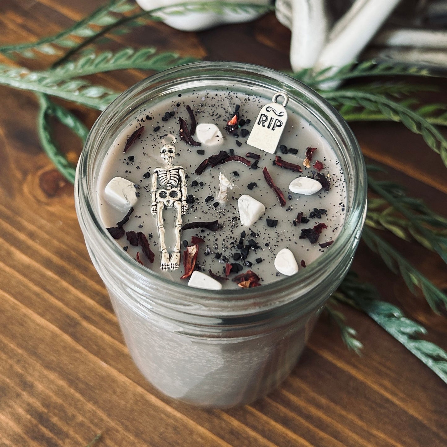 A dark Halloween candle that is decorated with a scary skeleton, a spooky rest in peace sign, white crystals, and gothic black glitter.