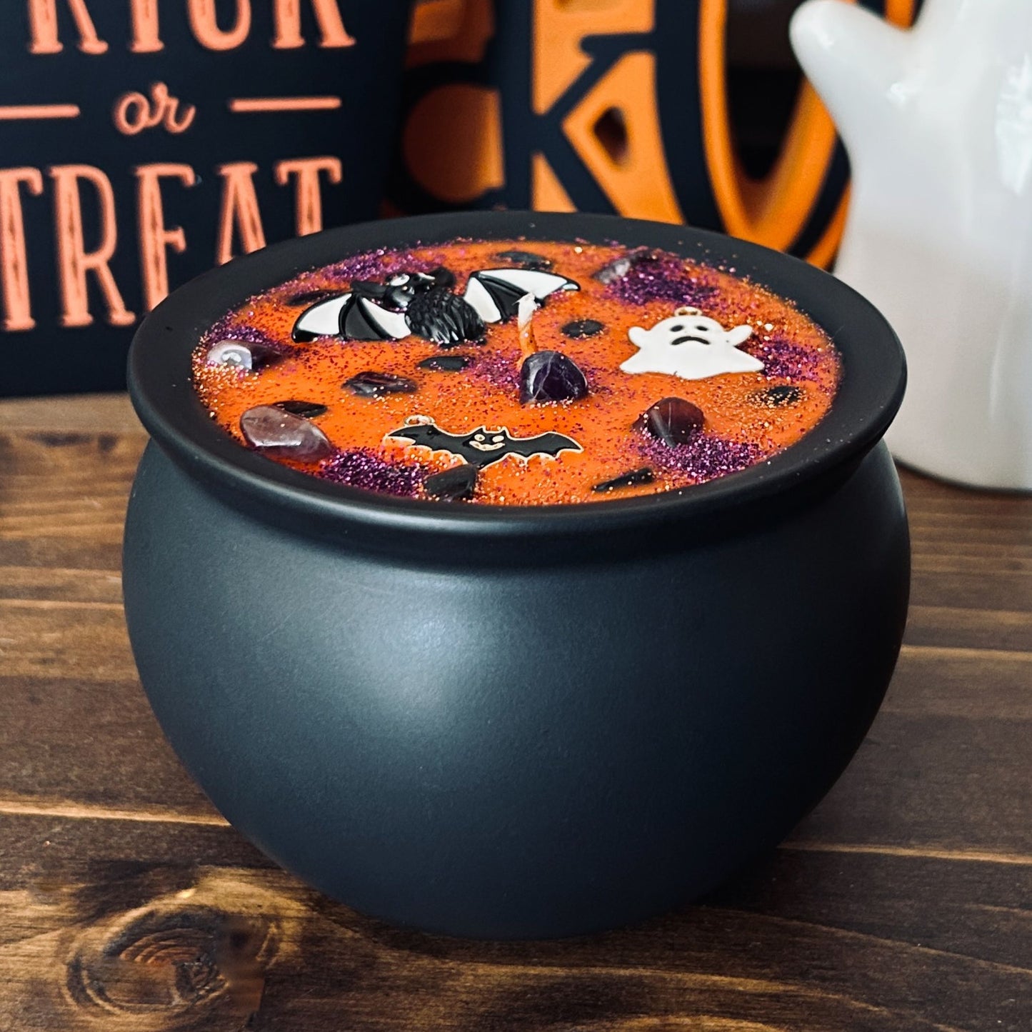 Orange Halloween candle in a black cauldron that is decorated with witchy crystals, spooky bats, and gothic glitter.
