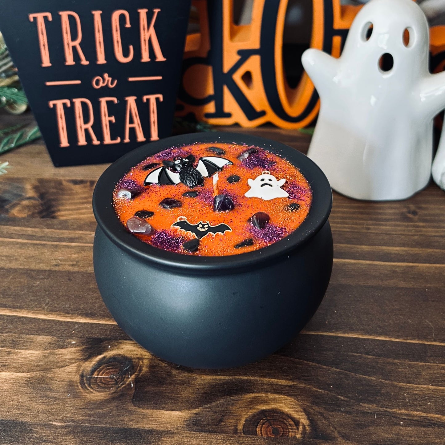 Orange Halloween candle in a black cauldron that is decorated with witchy crystals, spooky bats, and gothic glitter.
