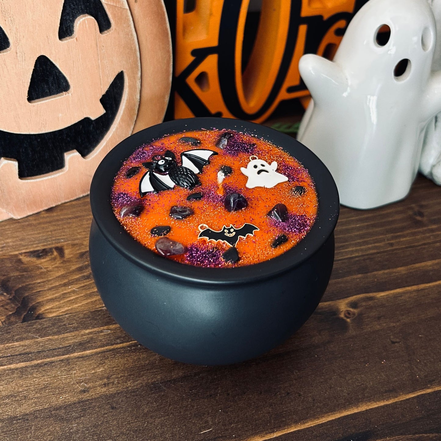 Orange Halloween candle in a black cauldron that is decorated with witchy crystals, spooky bats, and gothic glitter.