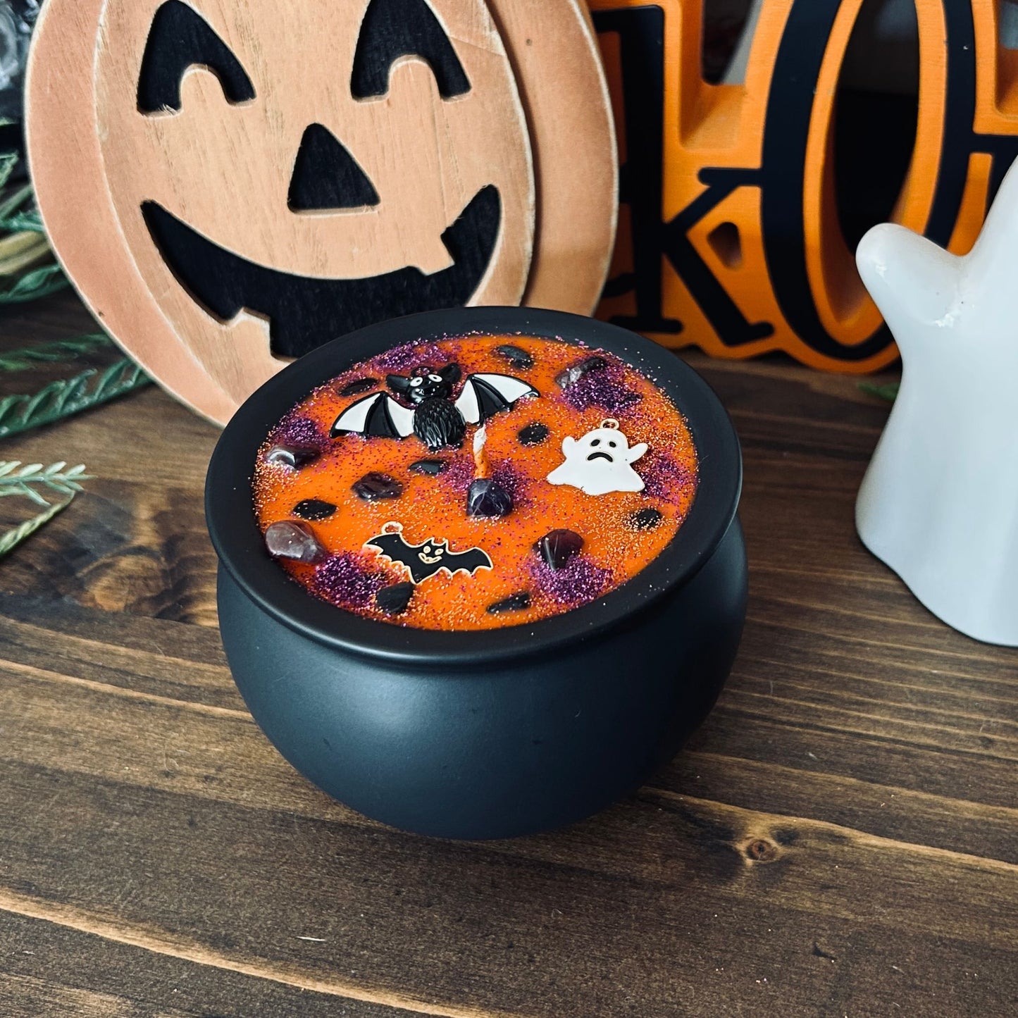 Orange Halloween candle in a black cauldron that is decorated with witchy crystals, spooky bats, and gothic glitter.