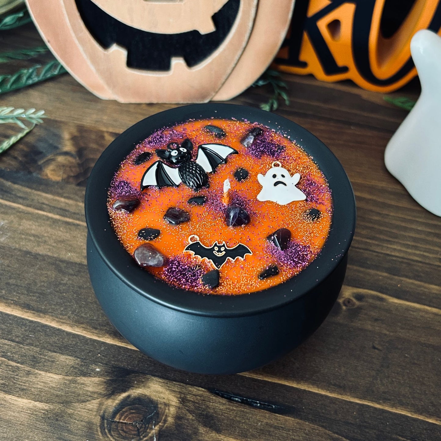 Orange Halloween candle in a black cauldron that is decorated with witchy crystals, spooky bats, and gothic glitter.