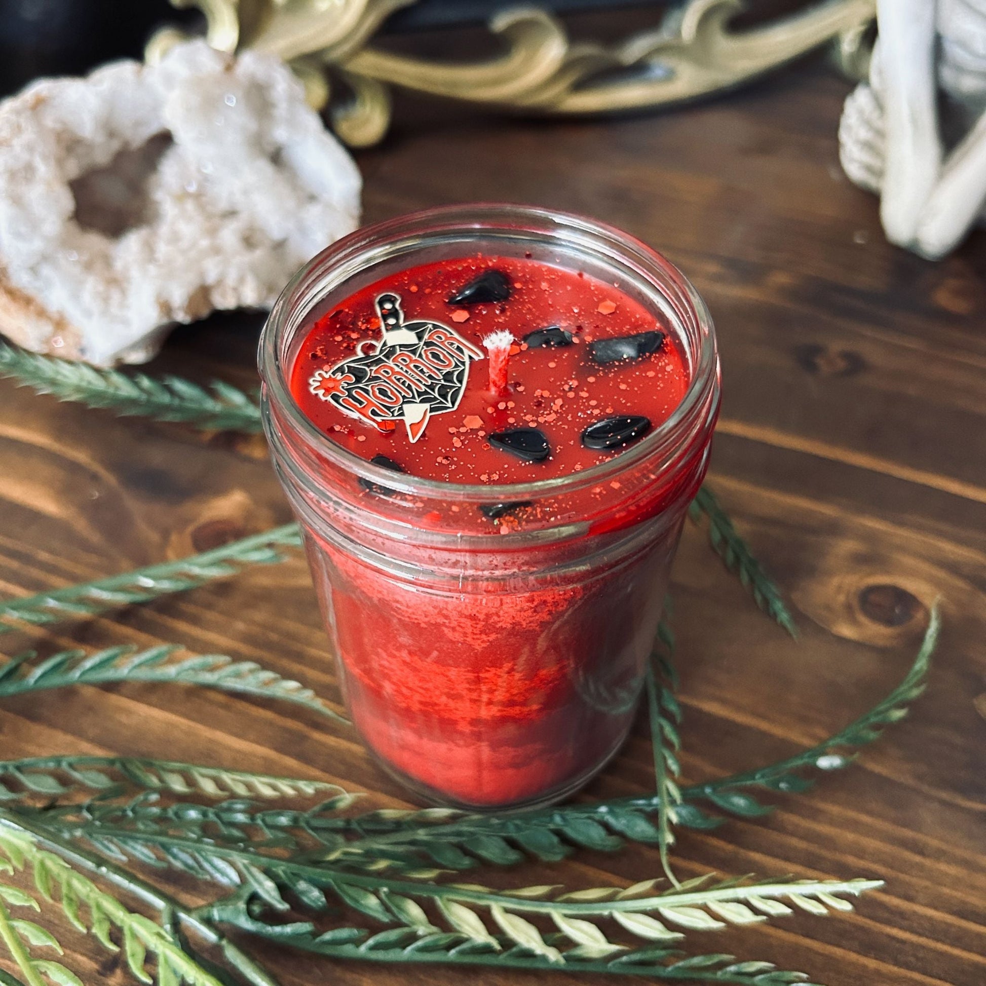 A red gothic candle that is decorated with a horror lover heart charm, spooky crystals, and gothic glitter.