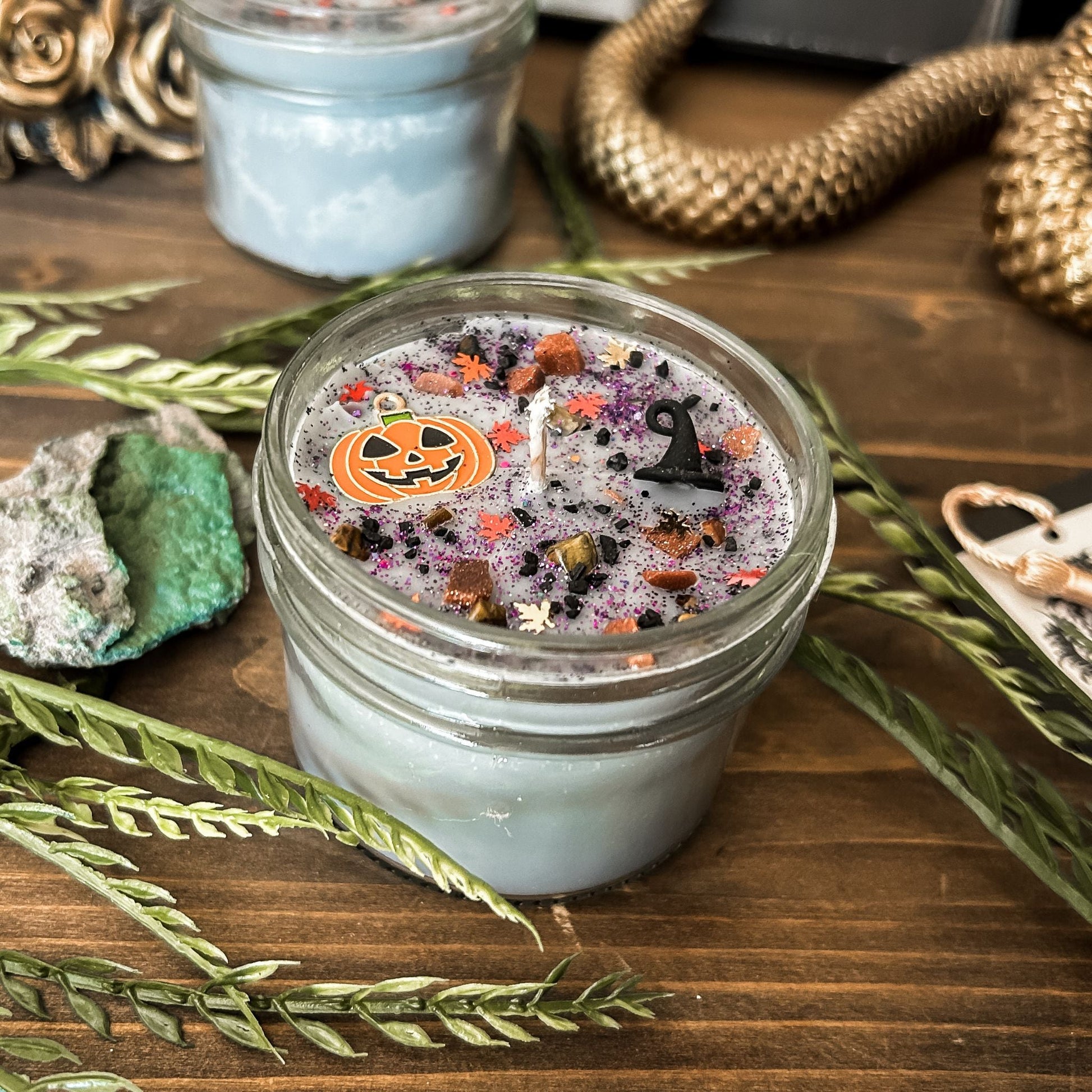 A Halloween candle that is decorated with a jack o lantern, a witch hat, spooky crystals, and autumn glitter.