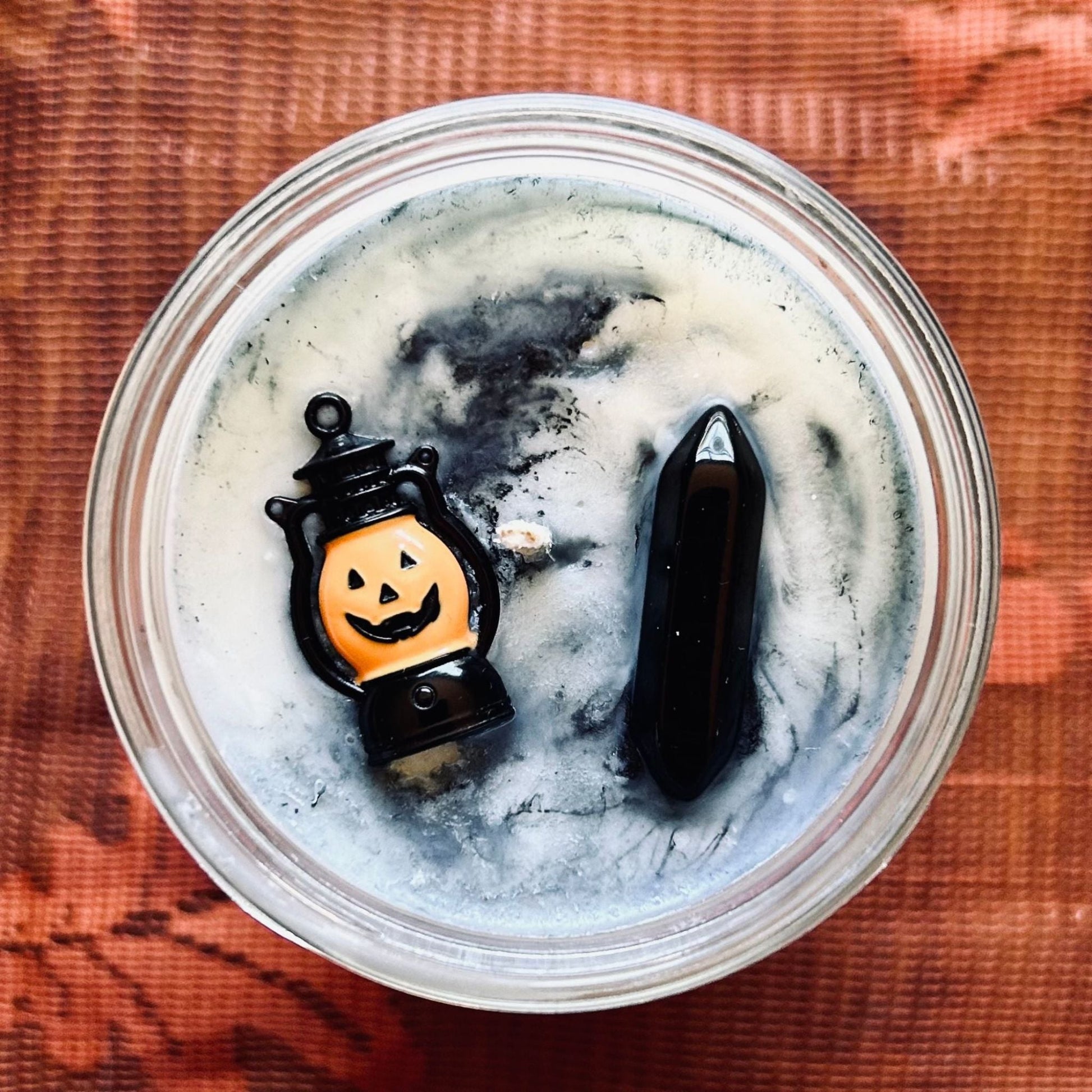 A white Halloween candle with black swirls. The candle is decorated with a spooky jack o lantern and a black obsidian crystal.