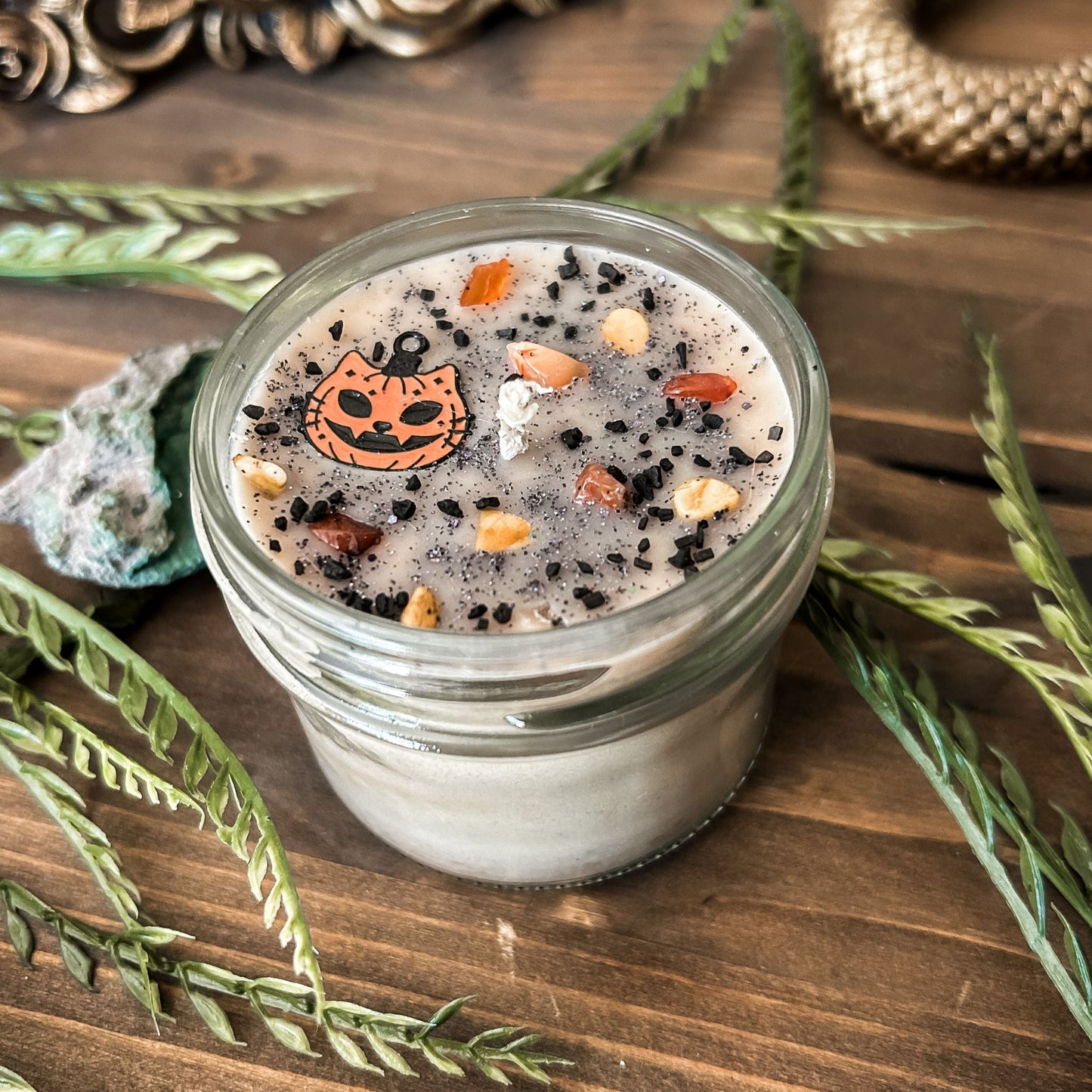 A vintage Halloween candle that is decorated with a spooky retro cat charm, witchy crystals, and spooky glitter.
