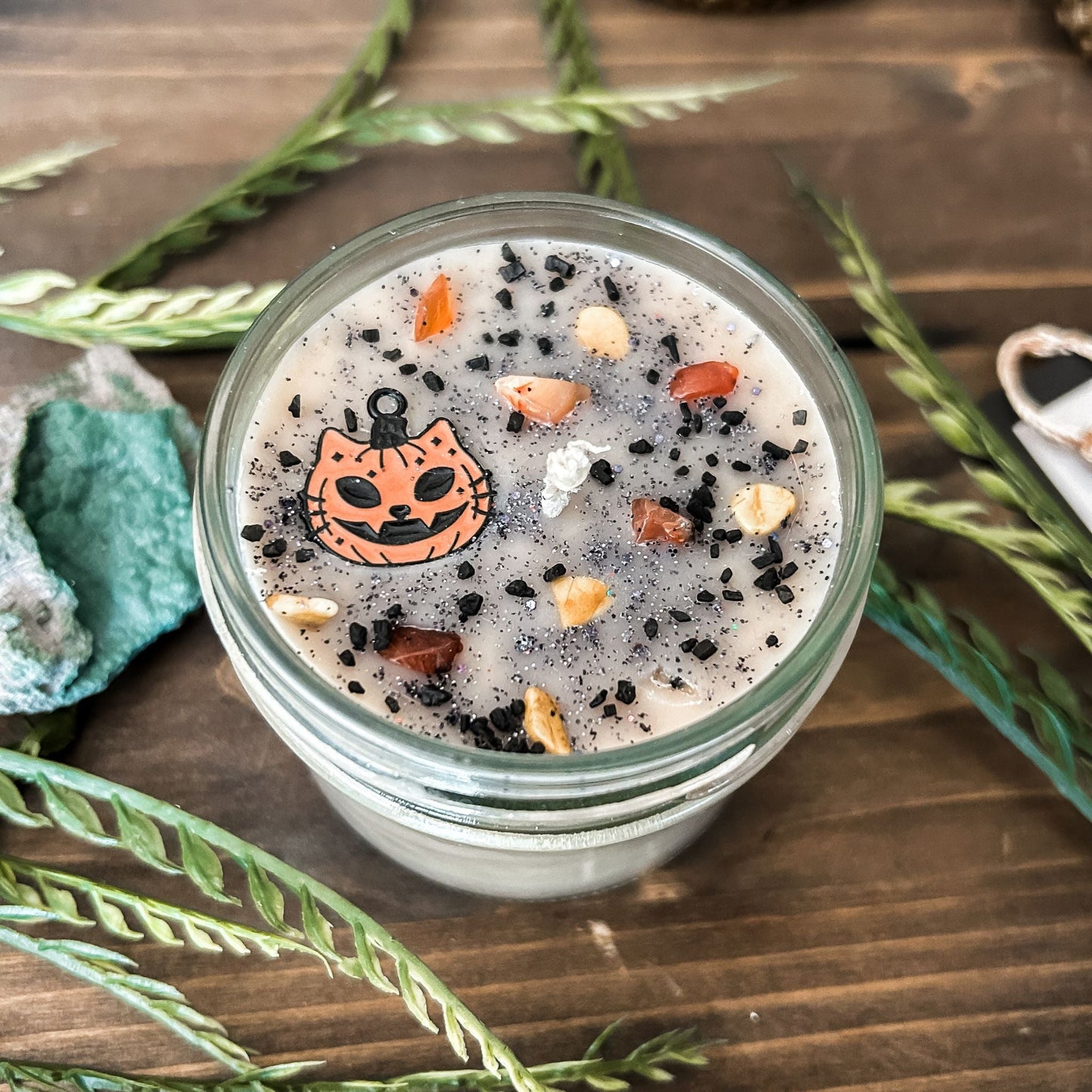 A vintage Halloween candle that is decorated with a spooky retro cat charm, witchy crystals, and spooky glitter.