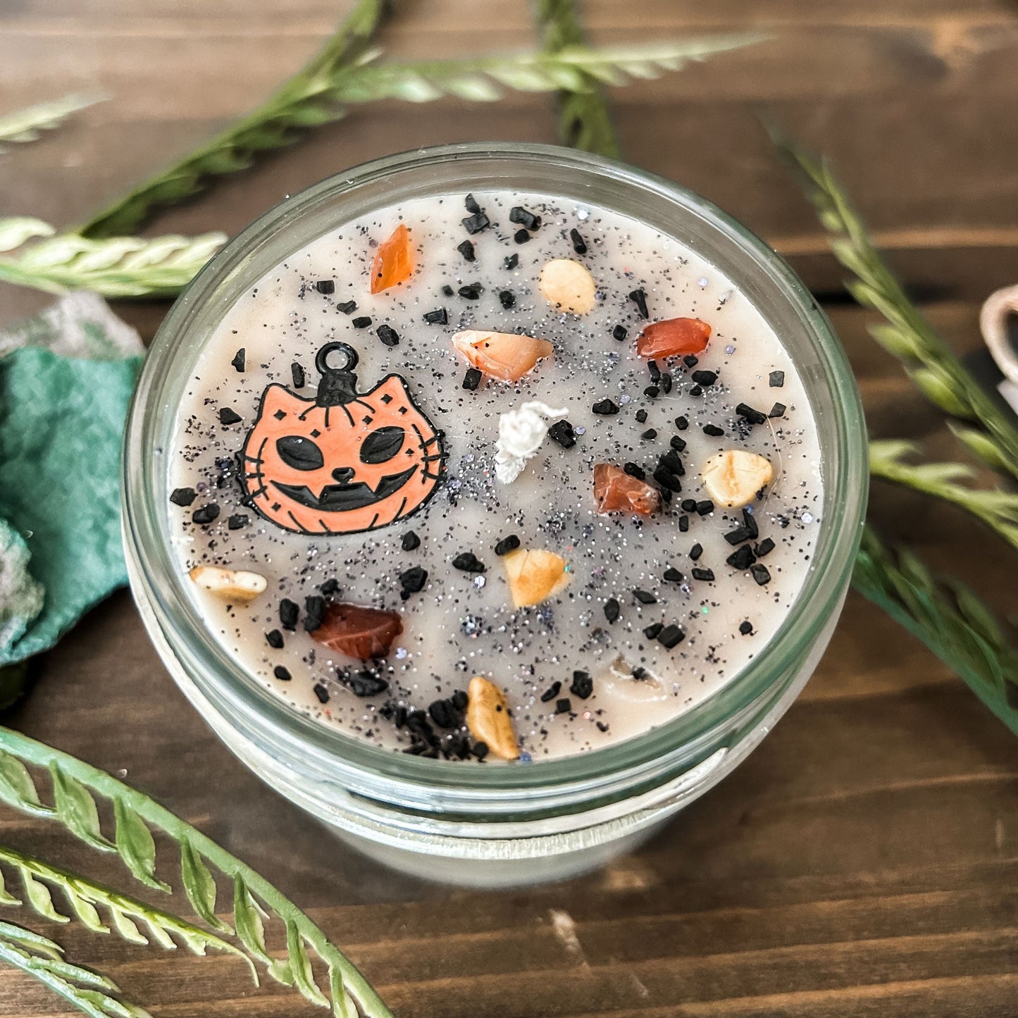 A vintage Halloween candle that is decorated with a spooky retro cat charm, witchy crystals, and spooky glitter.