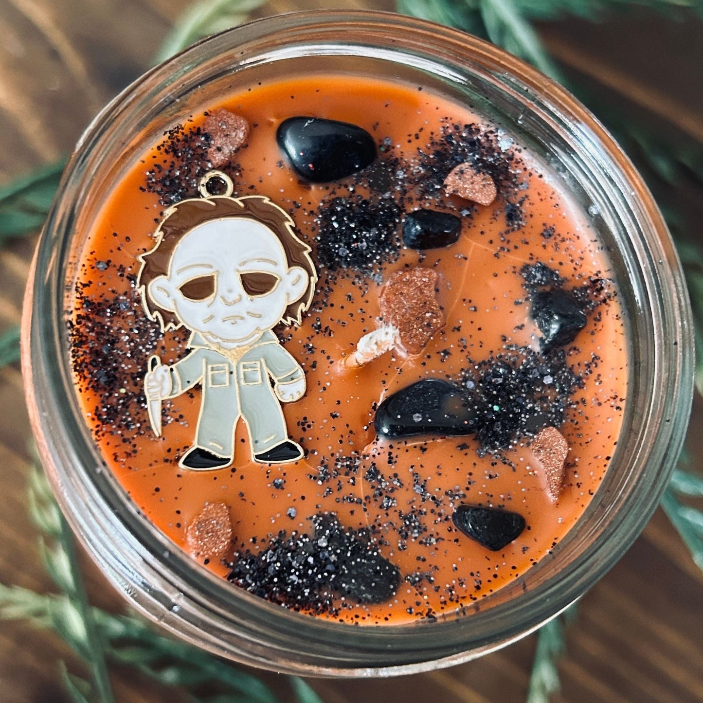 An Orange Halloween candle that is decorated with a Michael Myers horror movie character, spooky crystals, and creepy glitter.