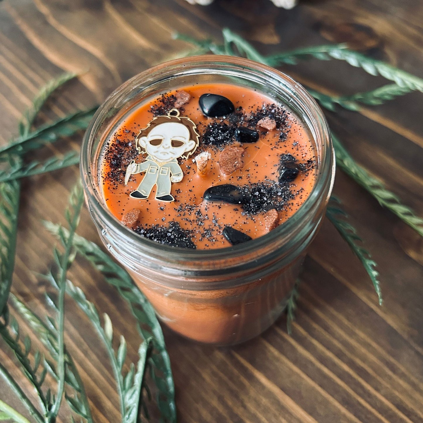 An Orange Halloween candle that is decorated with a Michael Myers horror movie character, spooky crystals, and creepy glitter.