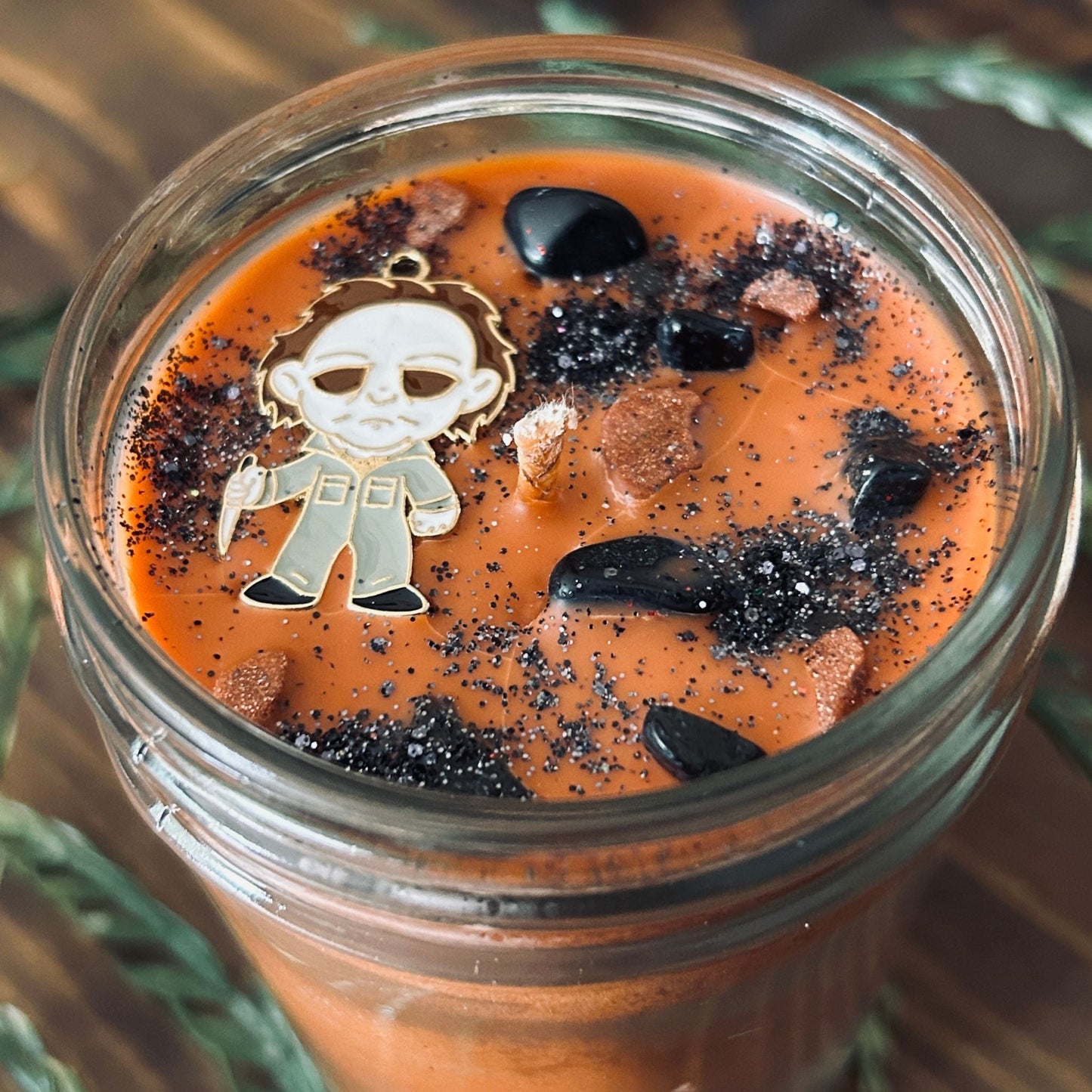 An Orange Halloween candle that is decorated with a Michael Myers horror movie character, spooky crystals, and creepy glitter.