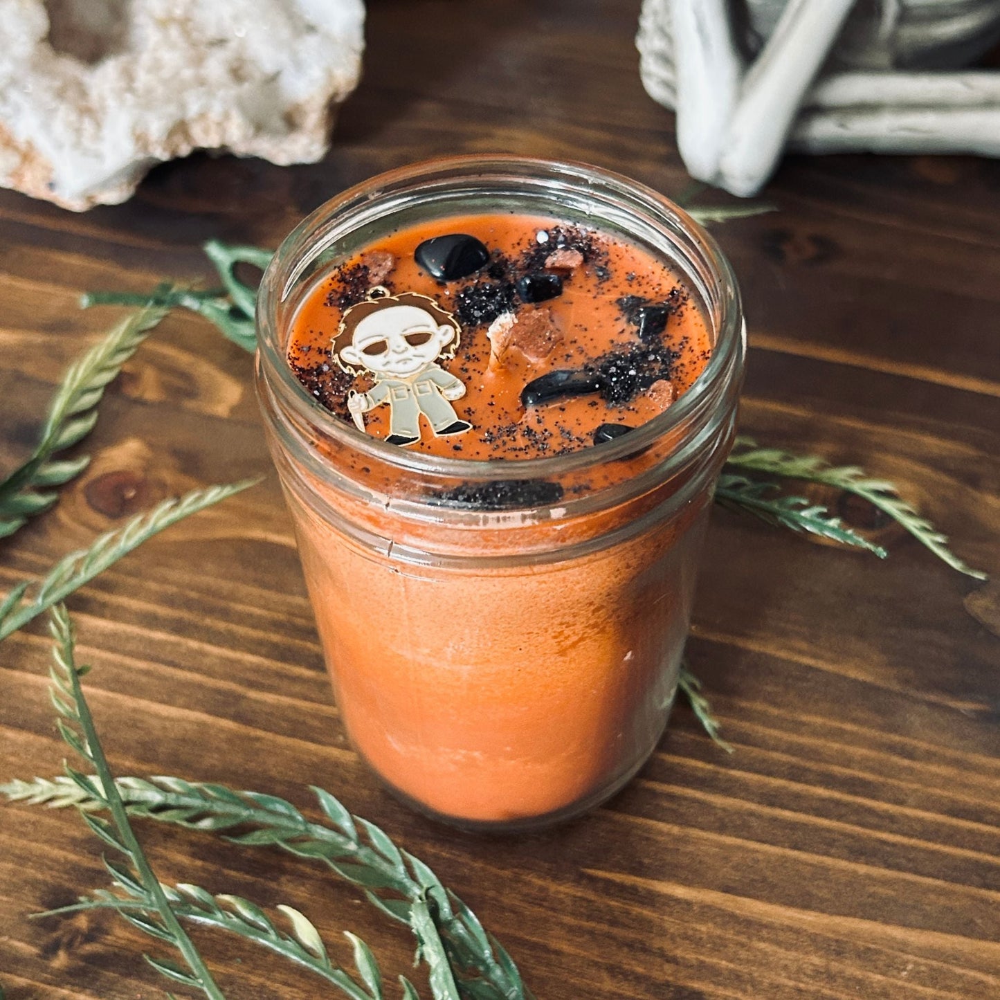 An Orange Halloween candle that is decorated with a Michael Myers horror movie character, spooky crystals, and creepy glitter.