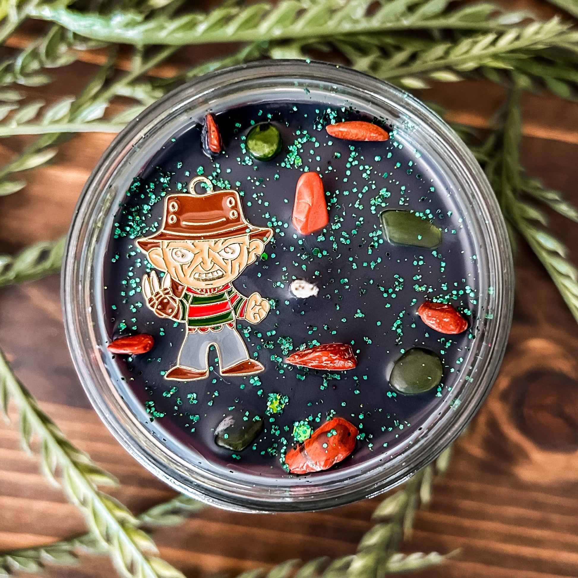 A black Halloween candle that is decorated with a horror movie charm, spooky crystals, and gothic glitter.
