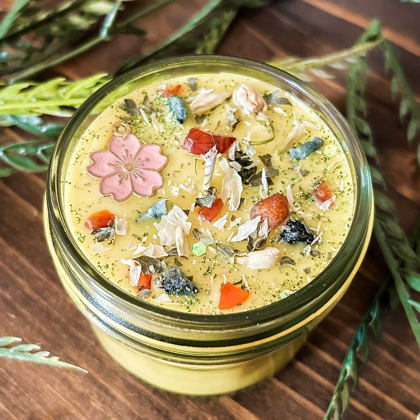 yellow intention pagan candle that is decorated with a pink flower, crystals, flowers, and magic glitter. The candle represents Beltane and is for setting intentions for renewal, positive energy, purity, and fertility.