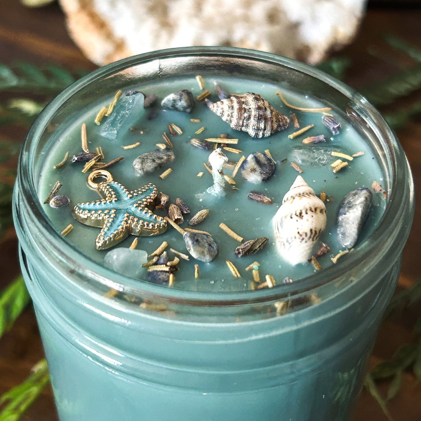 Seafoam green intention candle that is decorated with a starfish, seashells, herbs, and witchy glitter for sea witch work and ocean magic rituals.