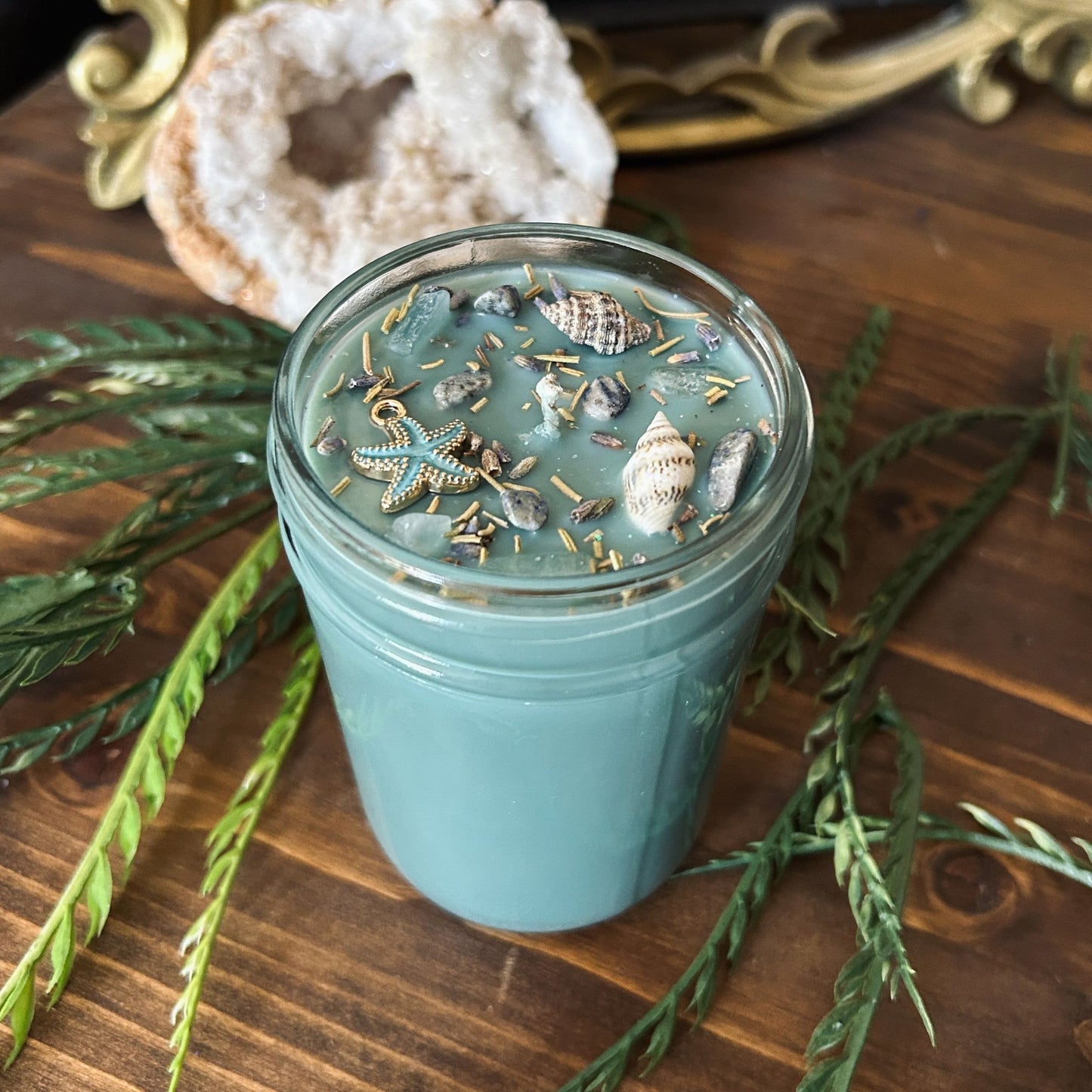 Seafoam green intention candle that is decorated with a starfish, seashells, herbs, and witchy glitter for sea witch work and ocean magic rituals.