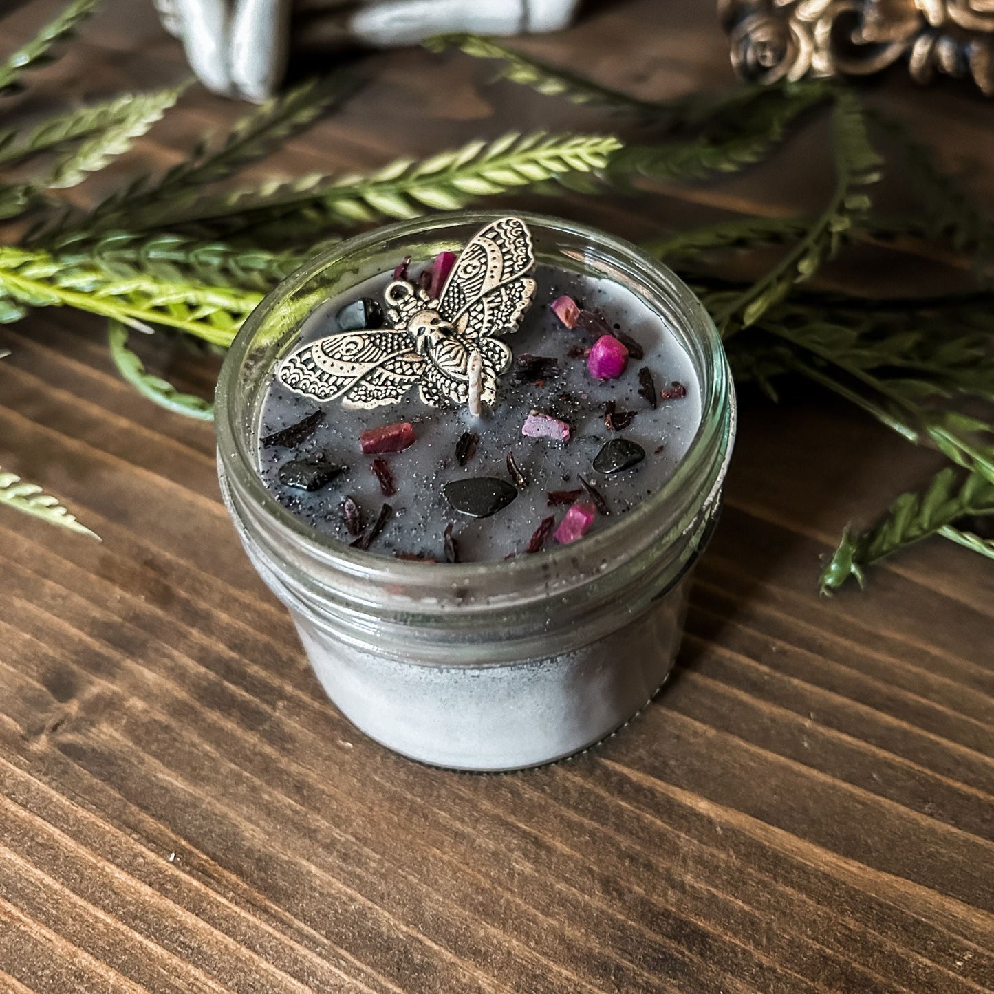 A gothic gray candle that is decorated with a gothic moth, spooky pink crystals, and dark glitter.