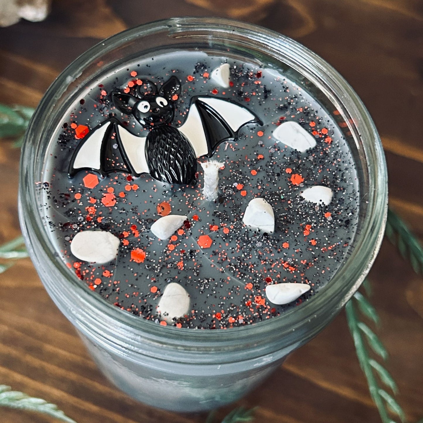 A gray Halloween candle that is decorated with a spooky black and white striped bat charm, white crystals, and gothic glitter.