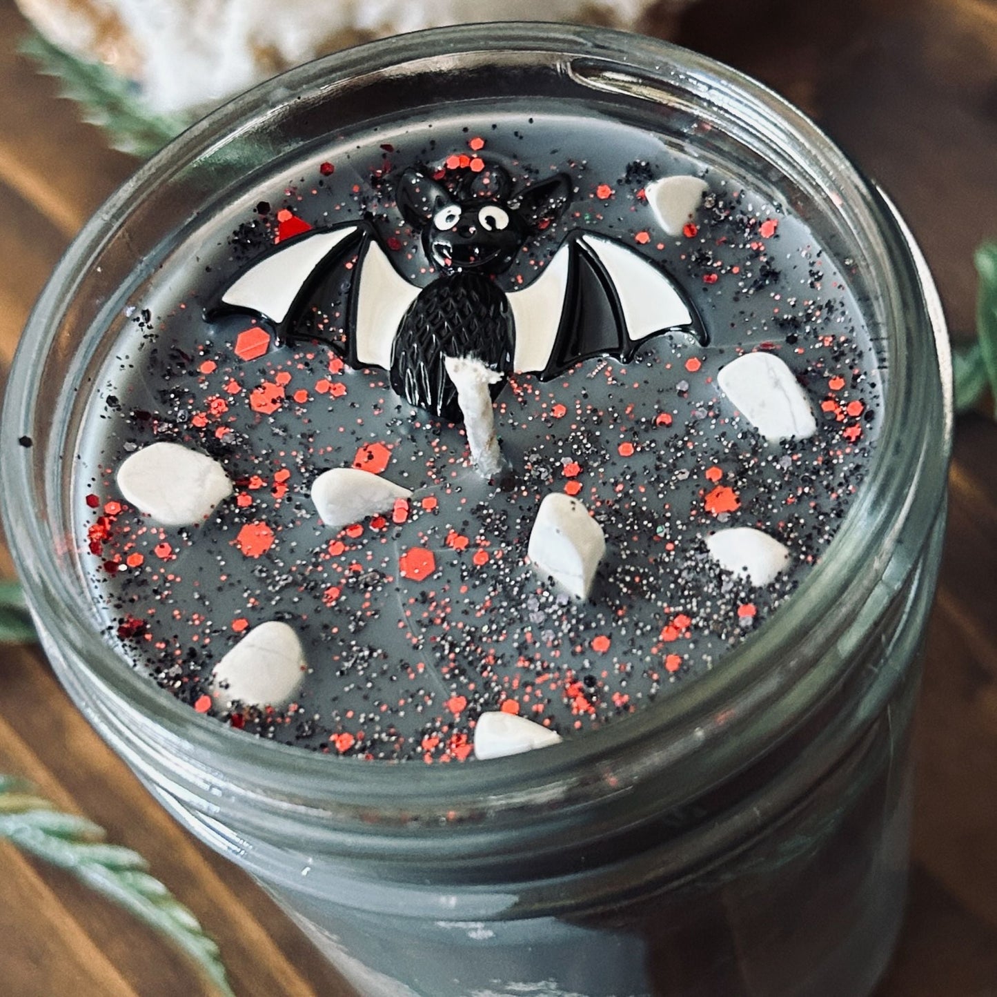 A gray Halloween candle that is decorated with a spooky black and white striped bat charm, white crystals, and gothic glitter.