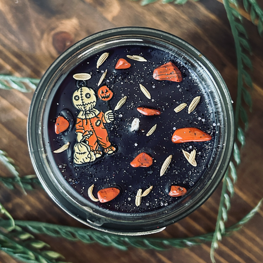 A black Halloween candle decorated with a spooky horror movie charm, witchy crystals, and gothic glitter.
