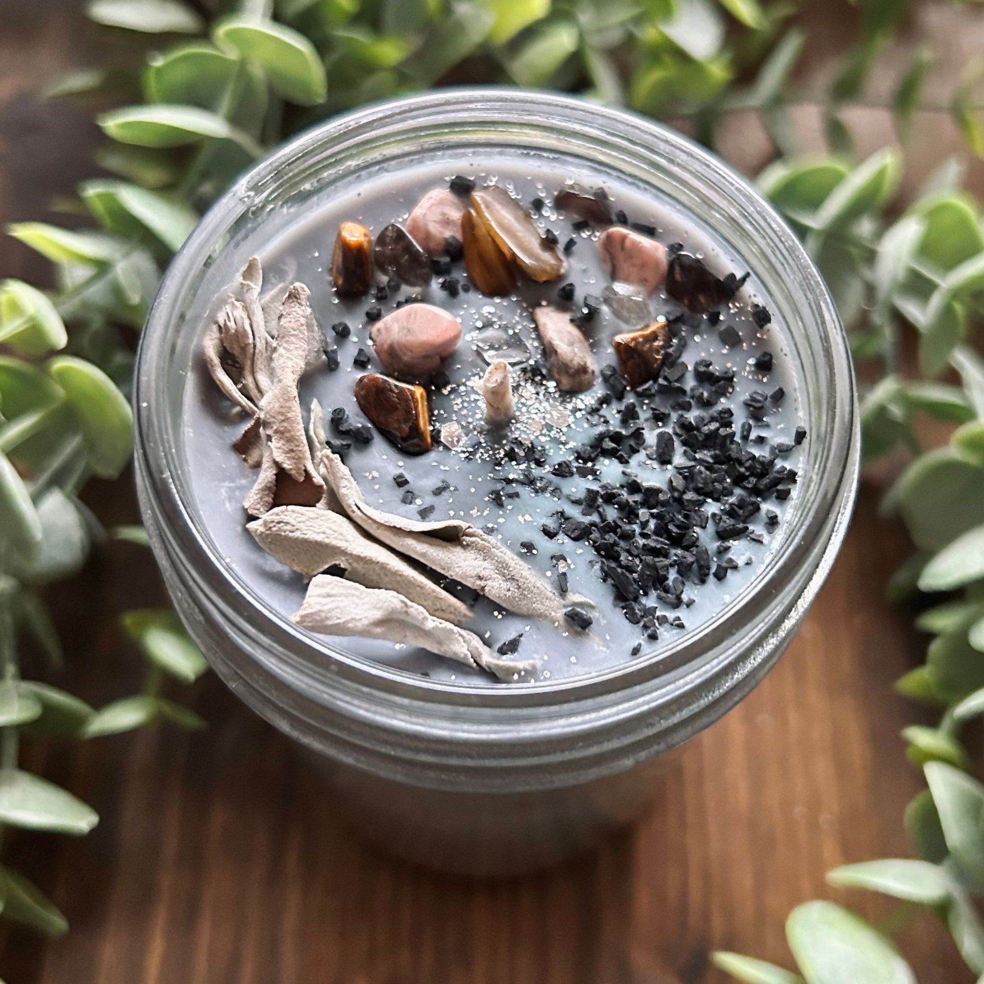 Silver intention candle that is decorated with gold tigers eye crystal, smokey quartz crystal, rhodonite crystal, protection salt, white sage, and witchy glitter to manifest goddess energy and power.