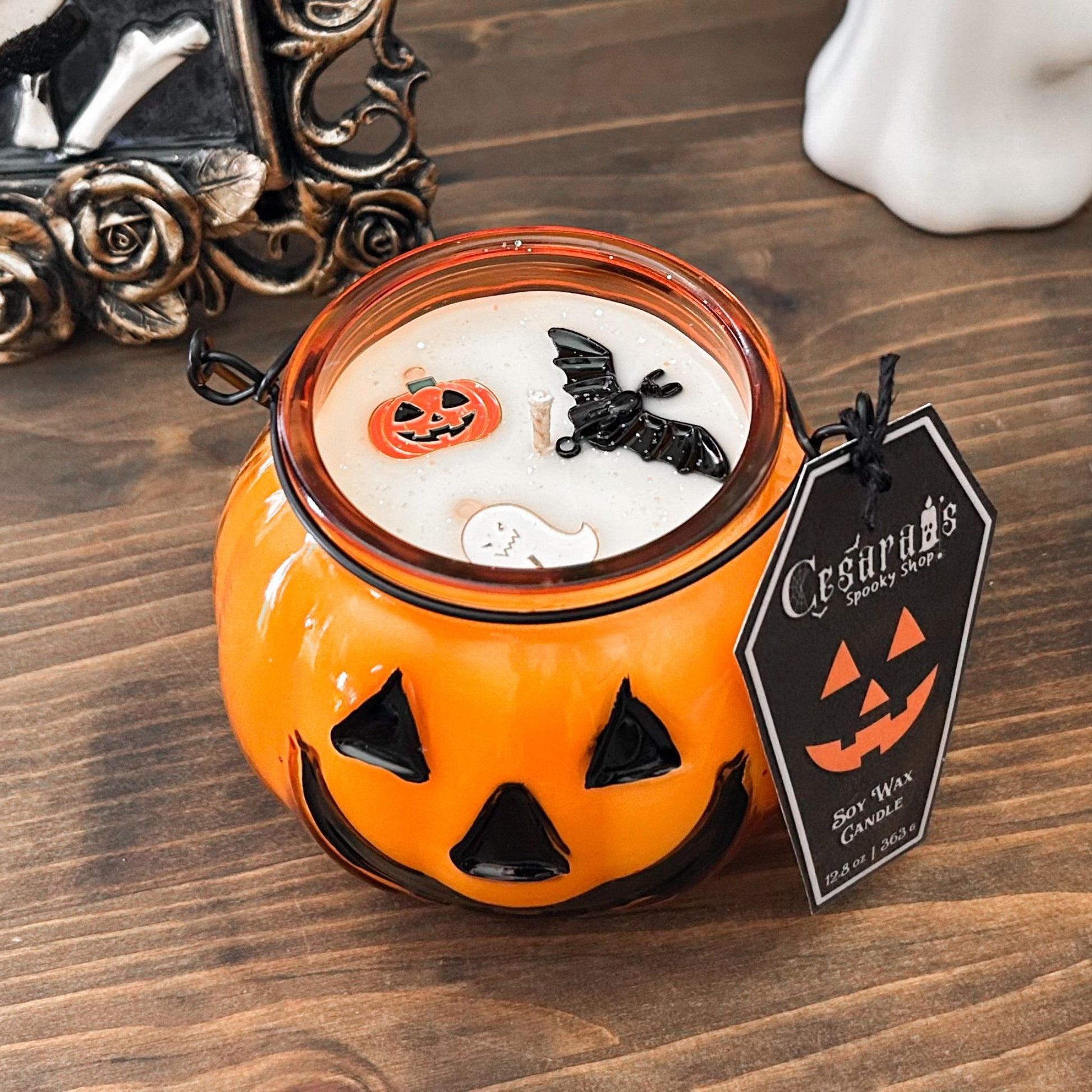 A Halloween candle in a jack o lantern that is decorated with a spooky bat, an autumn pumpkin, and a cute ghost.