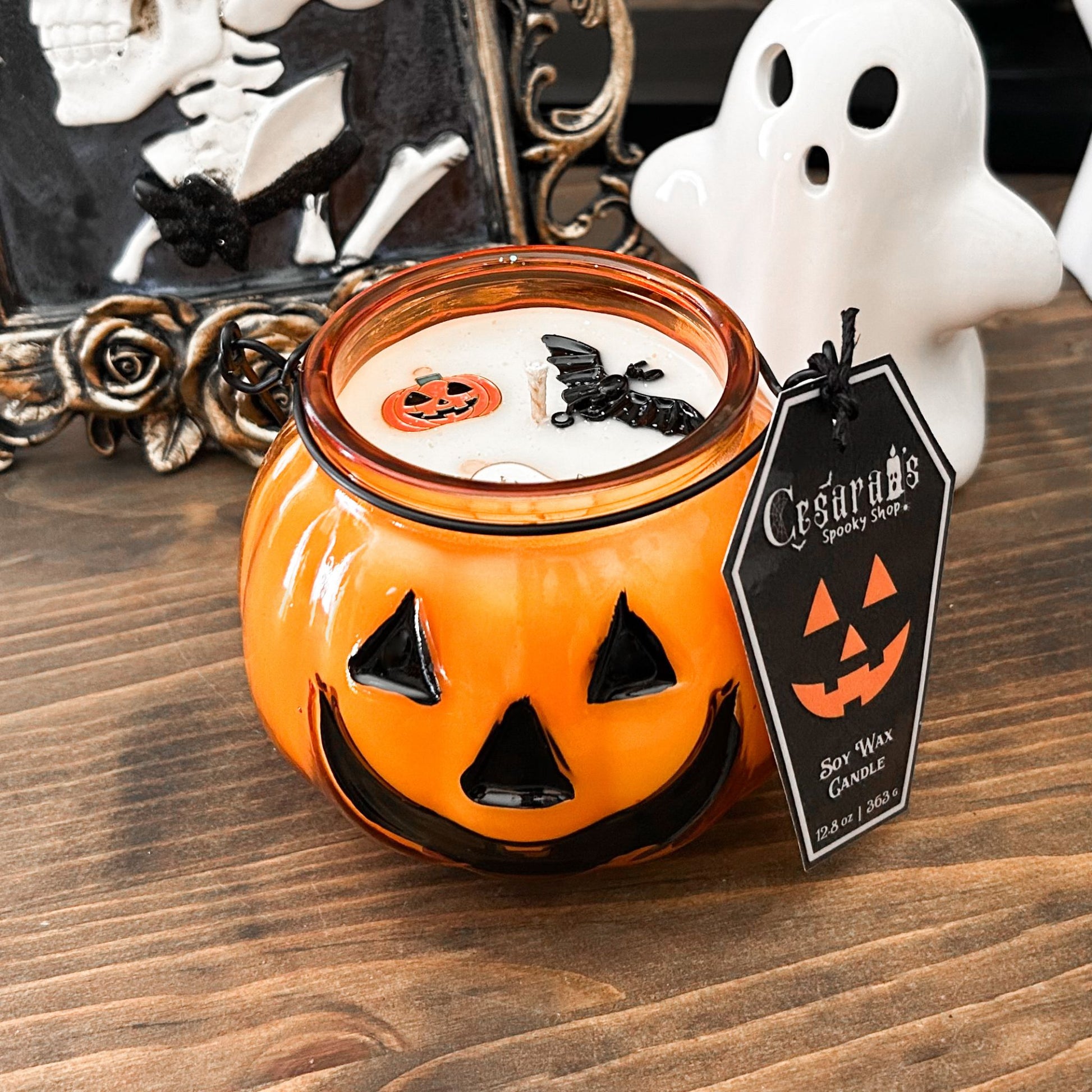 A Halloween candle in a jack o lantern that is decorated with a spooky bat, an autumn pumpkin, and a cute ghost.