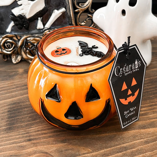 A Halloween candle in a jack o lantern that is decorated with a spooky bat, an autumn pumpkin, and a cute ghost.