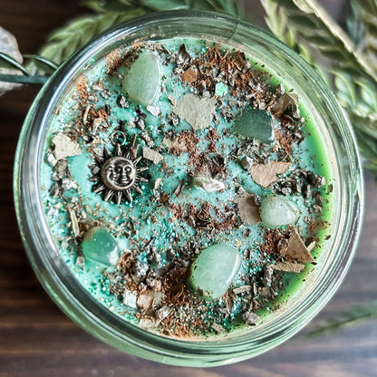 Green intention crystal candle that is decorated with a witchy sun and moon charm, gold magic glitter. The candle also has crystals and herbs for manifesting abundance.