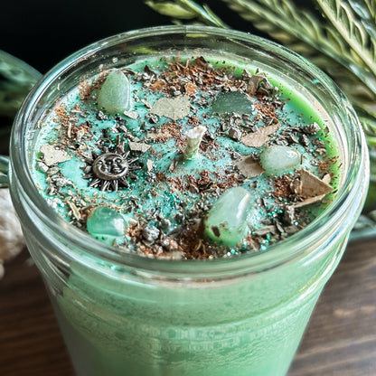Green intention crystal candle that is decorated with a witchy sun and moon charm, gold magic glitter. The candle also has crystals and herbs for manifesting abundance.
