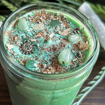 Green intention crystal candle that is decorated with a witchy sun and moon charm, gold magic glitter. The candle also has crystals and herbs for manifesting abundance.