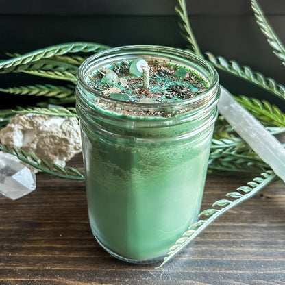 Green intention crystal candle that is decorated with a witchy sun and moon charm, gold magic glitter. The candle also has crystals and herbs for manifesting abundance.