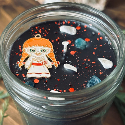 A black Halloween candle that is decorated with an Annabelle horror movie charm, spooky crystals, and paranormal glitter.