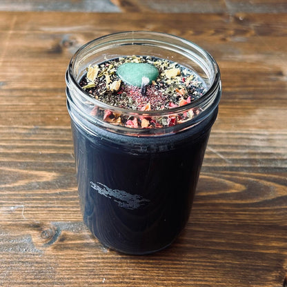 Black manifestation candle with a green aventurine heart shaped crystal, rose petals, jasmine, and glitter.