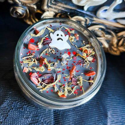A black Halloween candle with a spooky ghost, orange crystals, and autumn leaves.