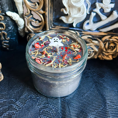 A black Halloween candle with a spooky ghost, orange crystals, and autumn leaves.