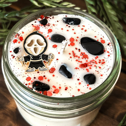 A Halloween candle decorated with a horror movie charm, spooky crystals, and gothic glitter.