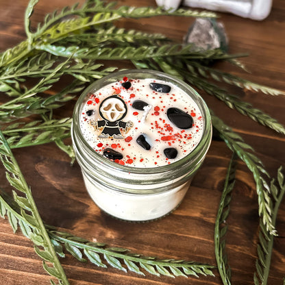 A Halloween candle decorated with a horror movie charm, spooky crystals, and gothic glitter.