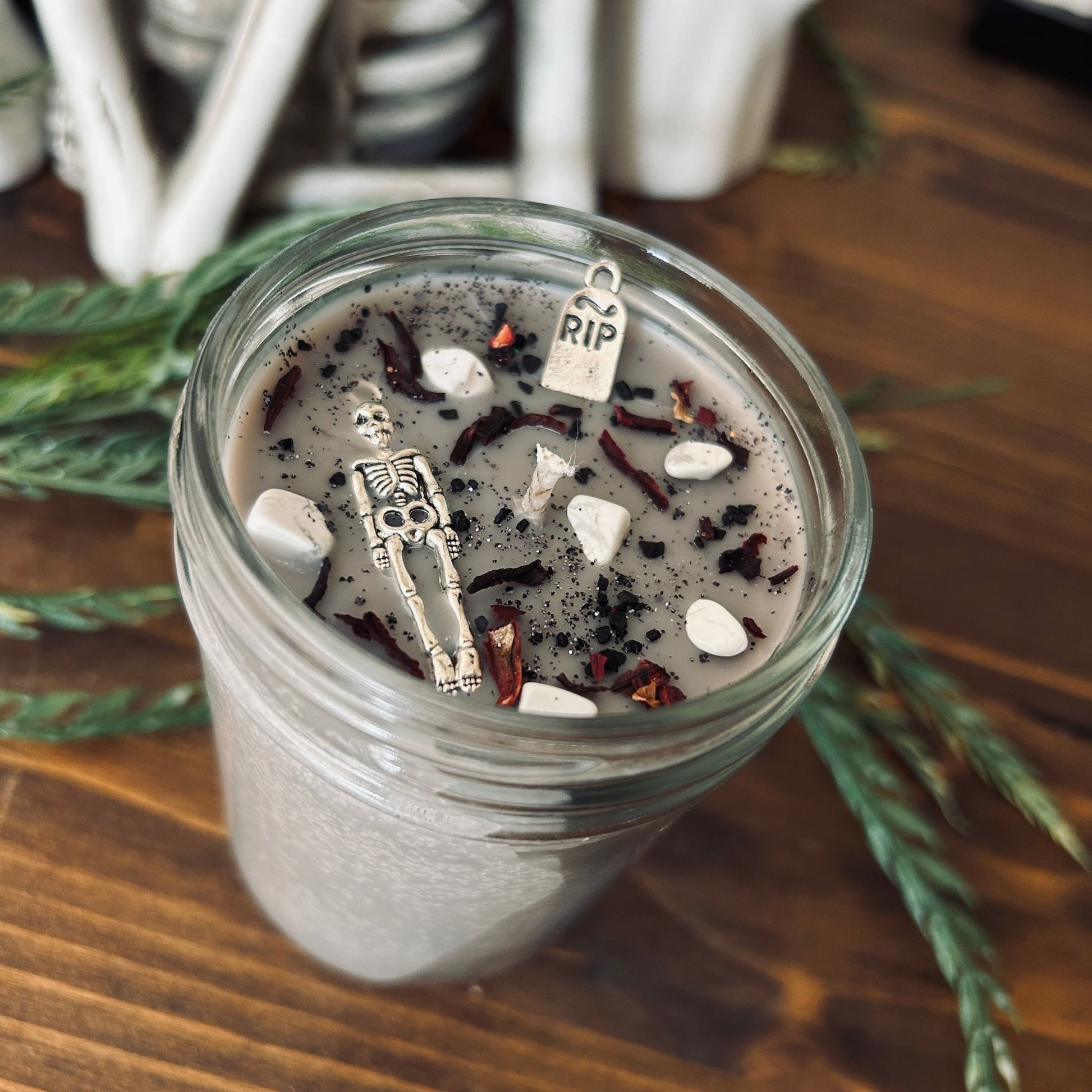 A dark Halloween candle that is decorated with a scary skeleton, a spooky rest in peace sign, white crystals, and gothic black glitter.